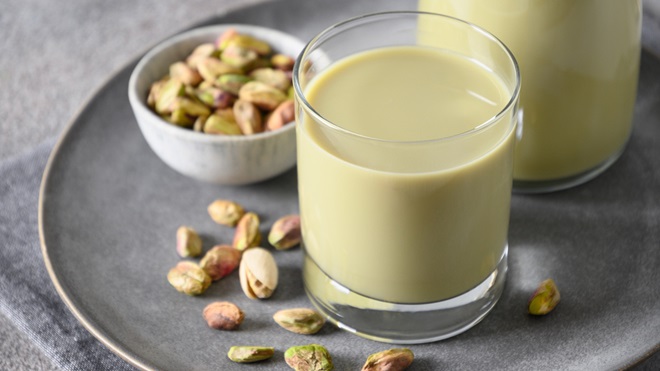 pistachio milk in a glass next to a bowl of pistachios